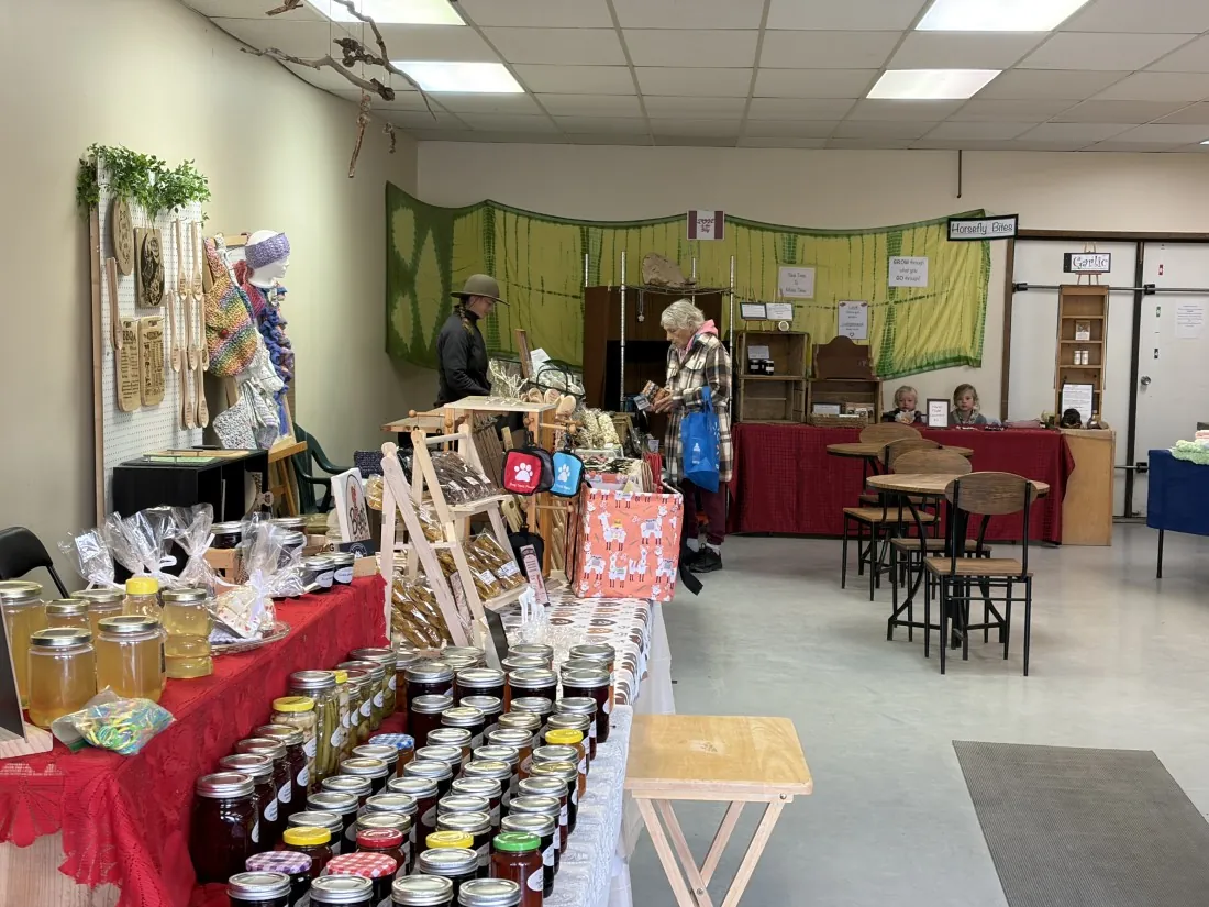 Inside the Horsefly Saturday Market hall: tables of honey and jam jars, craft displays, and shoppers browsing